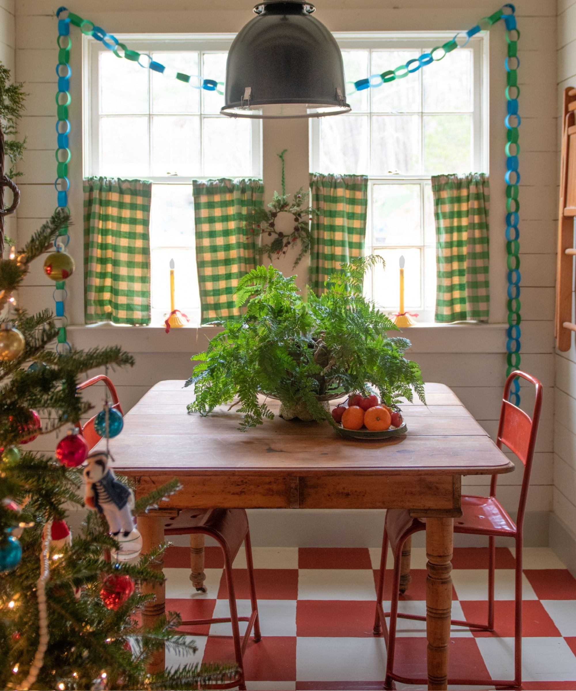 Dining room with old wooden table, checked cafe curtains, checked floor and paper chains