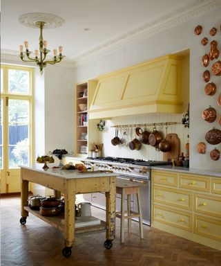 Kitchen with parquet flooring, white walls, yellow kitchen units, large kitchen range and central table island on wheels.