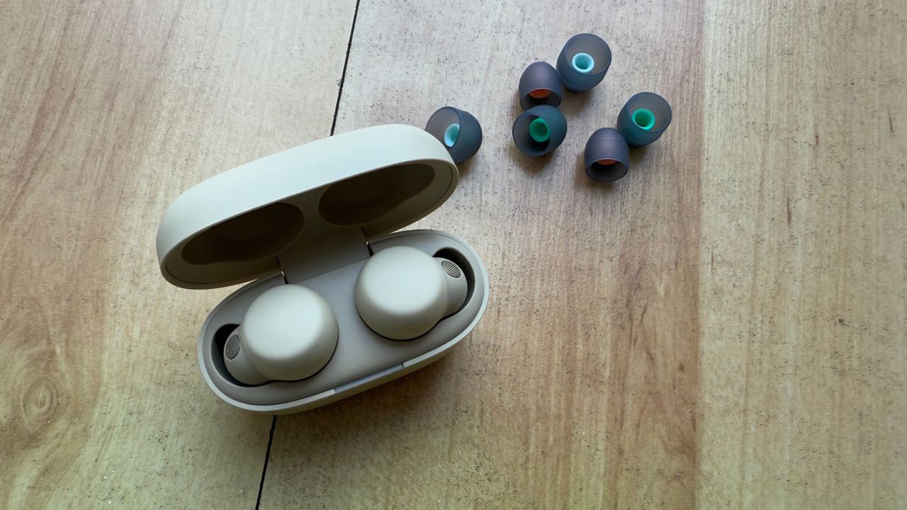 A pair of Sony Linkbuds S in their charging case on a wooden table, with additional silicone ear tips sitting slightly behind them.