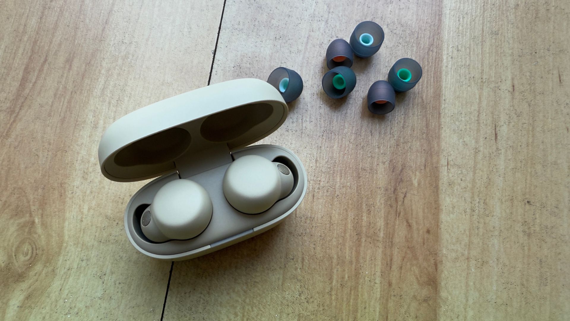 A pair of Sony Linkbuds S in their charging case on a wooden table, with additional silicone ear tips sitting slightly behind them.