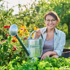 woman smiling in sunny garden with watering can