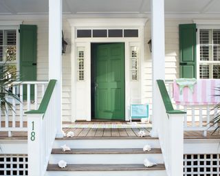 A wooden front porch on a house with white siding and a green front door