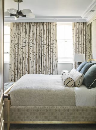 neutral bedroom with linear print drapes, gold edged bed, teal pillows, taupe blanket, pendant light
