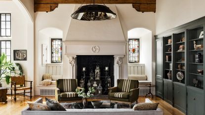 Living room with green built-in bookshelves, two striped green armchairs, an ornate wall with stained glass windows, and miscellaneous flowers and ornaments.
