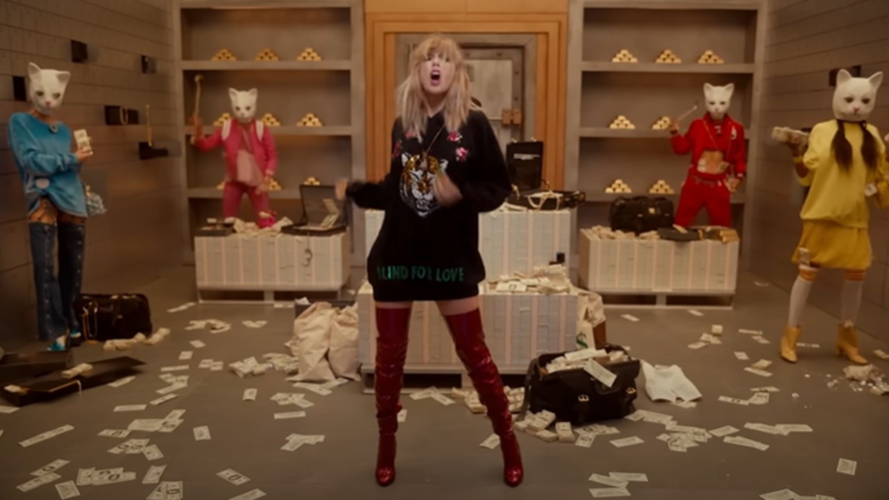 Taylor Swift de pie en una caja fuerte en "Mira lo que me hiciste hacer" Vídeo musical. Lleva un suéter negro y botas rojas hasta el muslo.