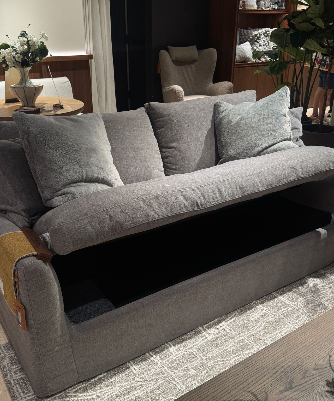 gray sofa with cushions and the seat lifted up to reveal storage on gray rug with timber coffee table