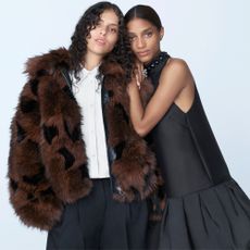 Two models one wearing a brown fur coat and white shirt and the other wearing a drop waist black dress