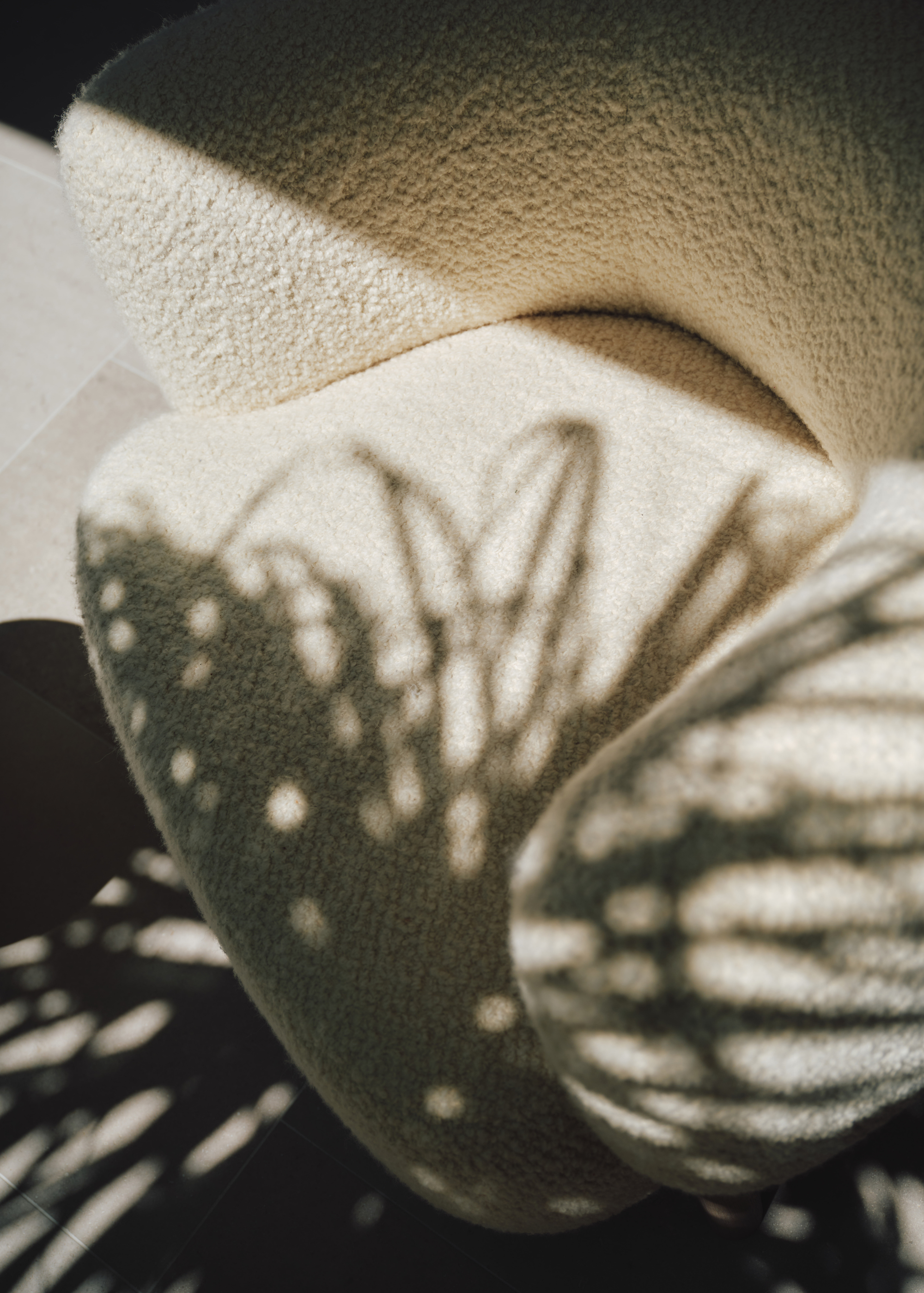 A close-up of an ivory boucle armchair with the shadow of a leaf
