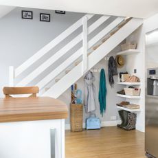 Area under the stairs filled with coats on coat hooks and storage boxes on shelves
