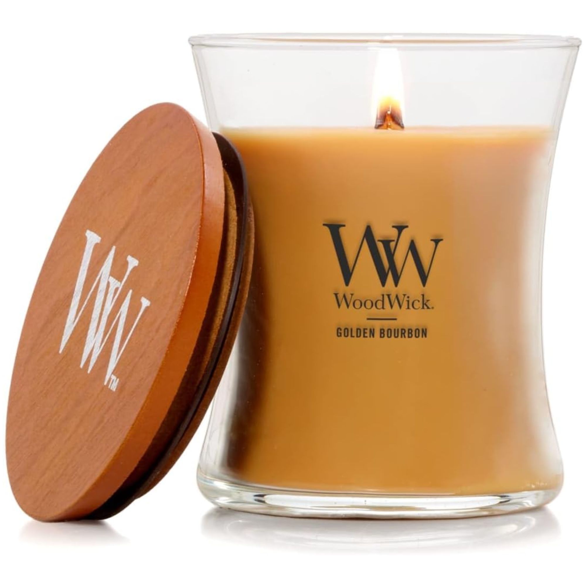 A lit WoodWick golden bourbon candle with a dark wood lid leaning against it