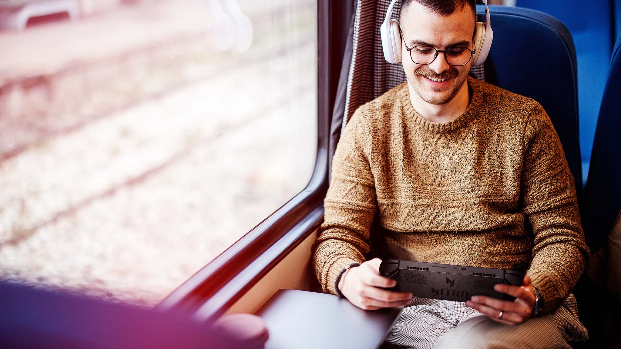 A man playing an Acer Nitro Blaze 8 on a train.