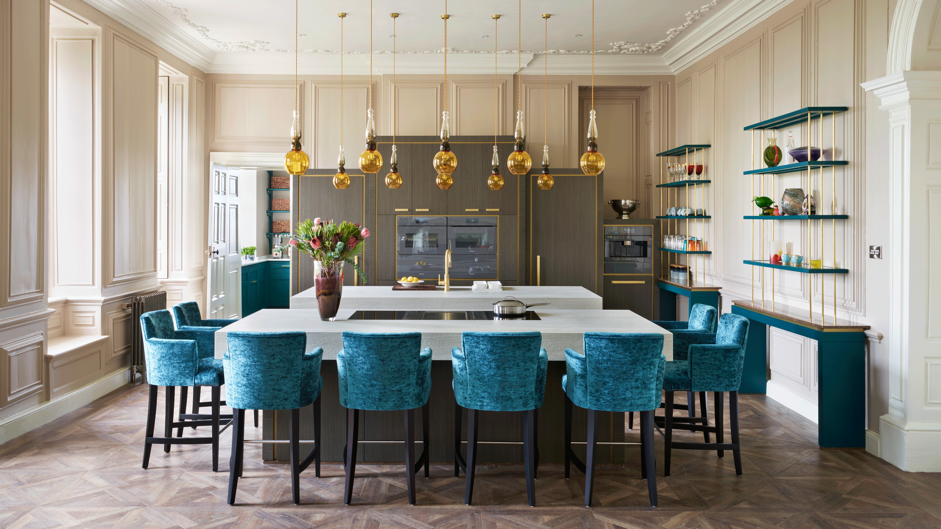 Wooden parquet illustrating the best kitchen flooring in a large cream room with blue velvet chairs around an island with pendant lighting.
