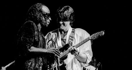 A classic black-and-white live shot of Robben Ford and Miles Davis performing together in 1986, with Ford playing a Fender Stratocaster.
