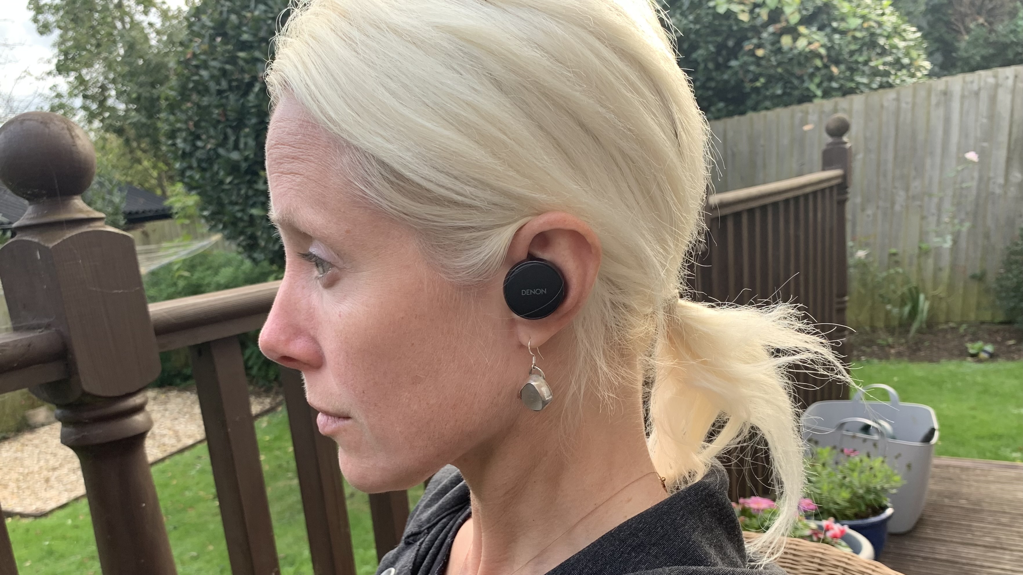 A woman in profile wearing the Denon PerL Pro outside, in a garden