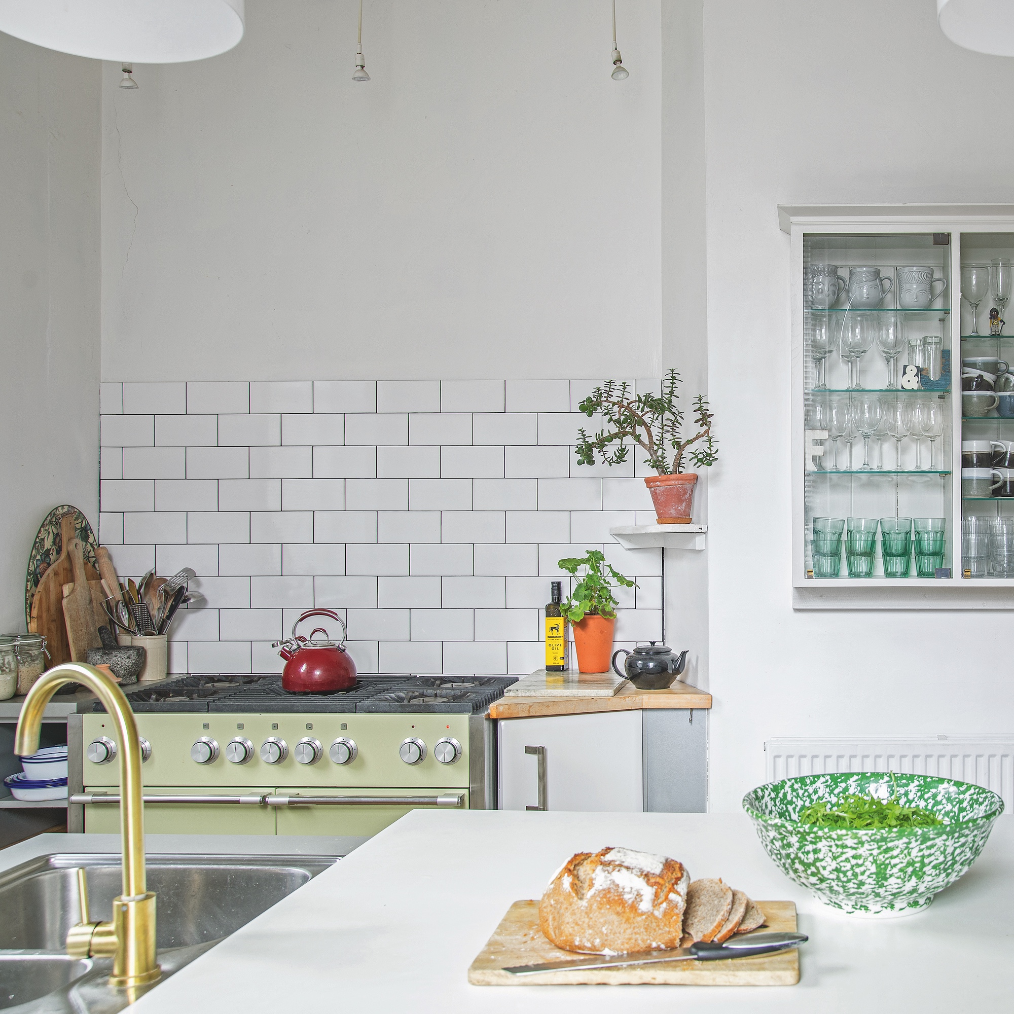 kitchen with white metro tiles, green range cooker, brass tap and wall cupboard with glasses inside