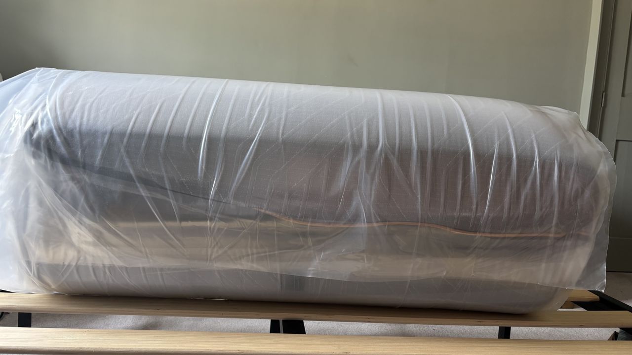 A vacuum-packed, rolled-up EGOHOME Black 12" Mattress fresh out of the box and place on a bed frame.