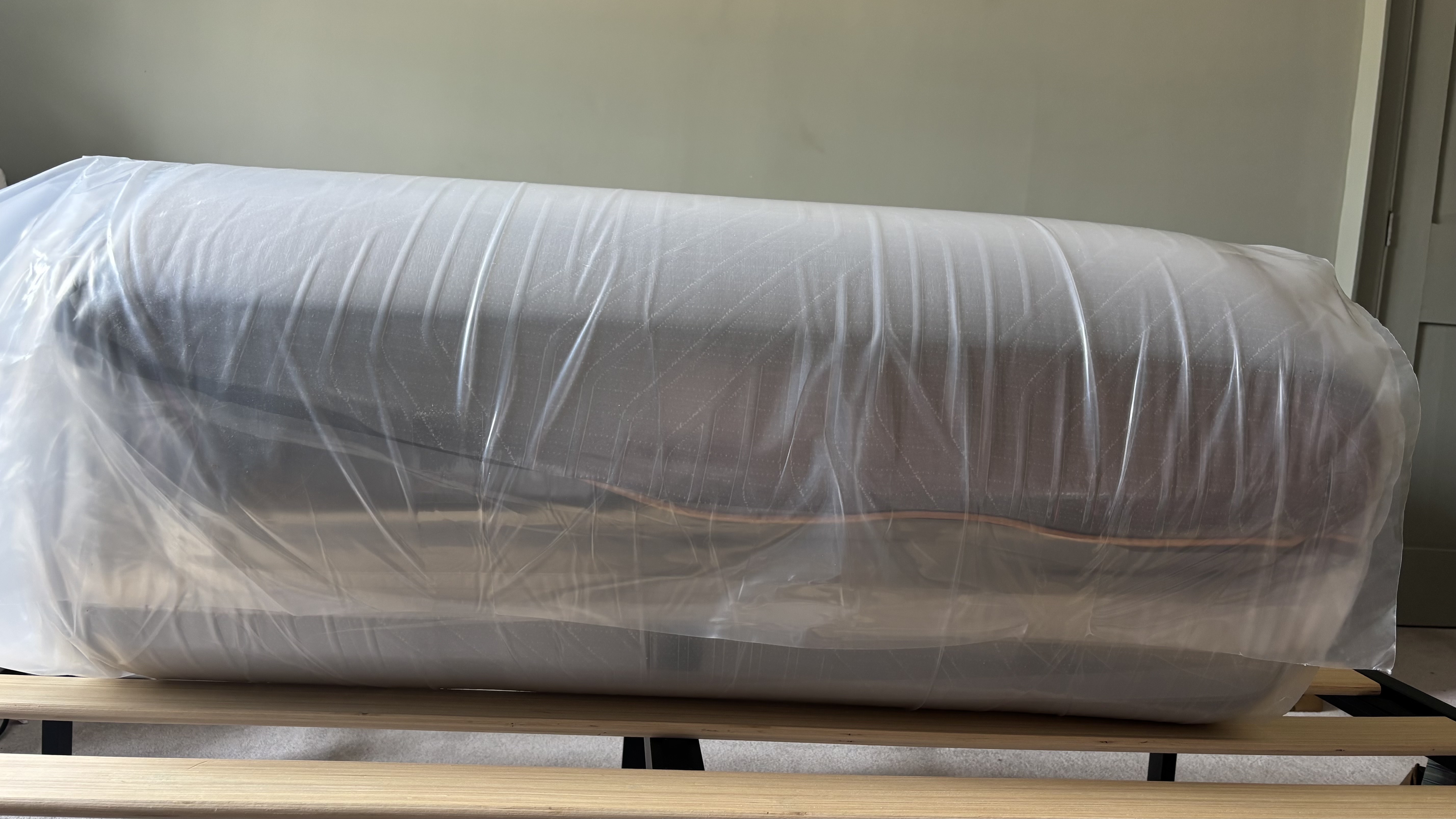 A vacuum-packed, rolled-up EGOHOME Black 12" Mattress fresh out of the box and place on a bed frame.