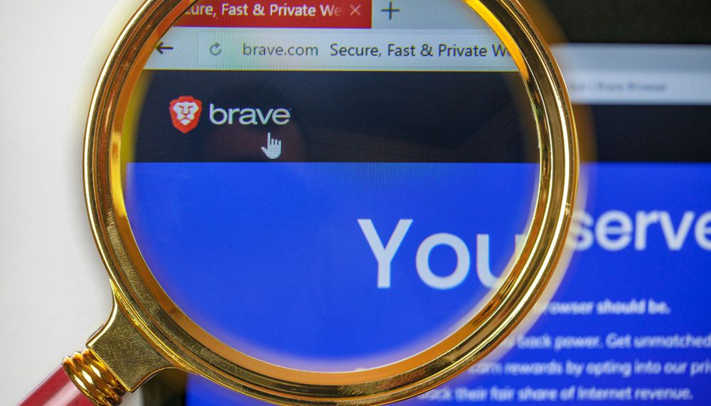 A magnifying glass highlighting the Brave logo in a browser window on a computer screen.