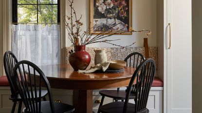 a cozy pattern layered dining nook with a banquette seat, small window and cafe curtain, wooden round table and black chairs