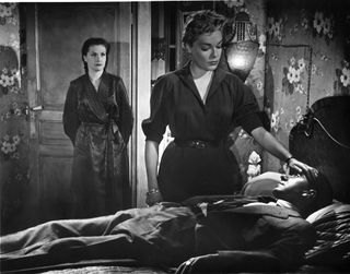 two women look over a sickly man in bed in Diabolique