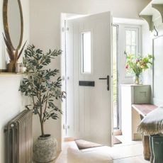 Hallway in a cottage-style house, with the white door open and a bench and plants inside the hallway