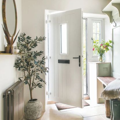Hallway in a cottage-style house, with the white door open and a bench and plants inside the hallway