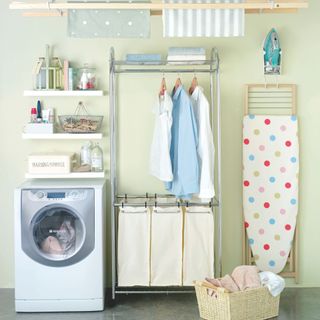 utility are with a washing machine, ironing board, washing basket, and shelves for accessories and cleaning products