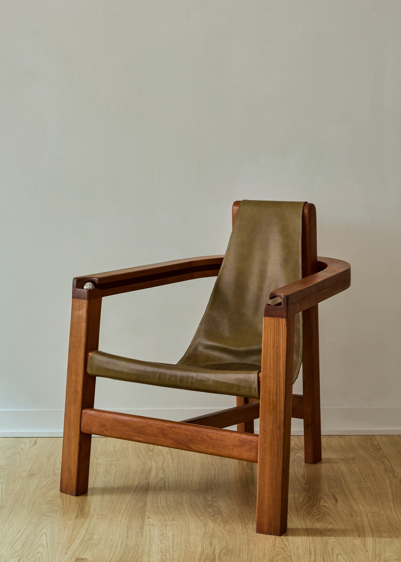 A wood chair with green leather-like seating and a metal fidget ball in a white room with wood flooring