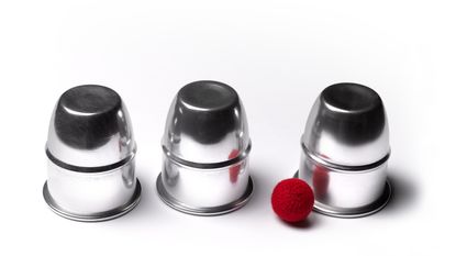 Three upside-down metal cups lined up next to a small red ball.