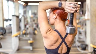 a woman doing a dumbbell overhead triceps extension in a gym