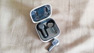 Amazon Echo Buds showing charging case with one earbuds outside of case on a beige background