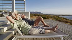 An older couple relax outside a luxurious beach house.