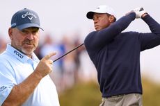 Tiger Woods in the finish position of his swing after hitting a tee shot with driver at the 152nd Open Championship, with an inset image of Thomas Bjorn appearing to point towards Tiger Woods