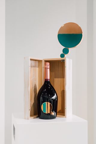 A bottle stands in front of a wooden box with a speech bubble above it