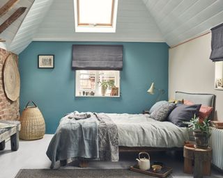 Bedroom in country cottage with modern twist, white painted floorboards, white paneled ceiling, blue painted walls, gray bedding and blinks, woven baskets and accessories, rustic wooden bed-frame and bench