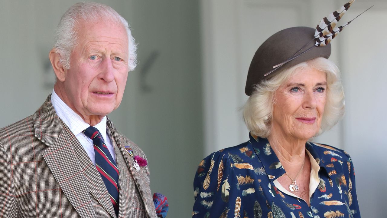 King Charles wears a a tweed suit and carries an umbrella while Queen Camilla wears a blue suit with a feather-print