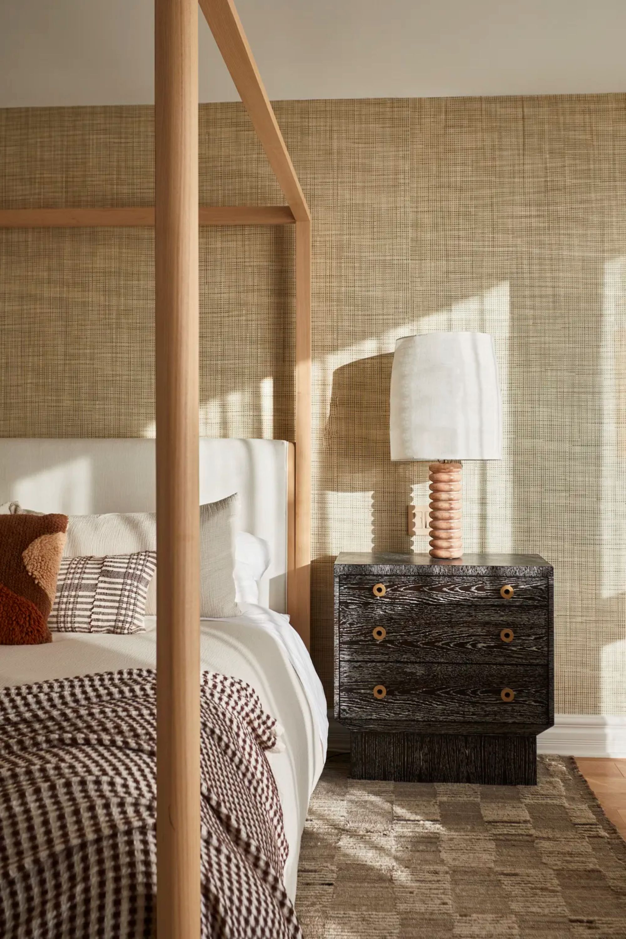 modern bedroom with jute rug, canopy bed, grasscloth wallpaper, black bedside table with lamp