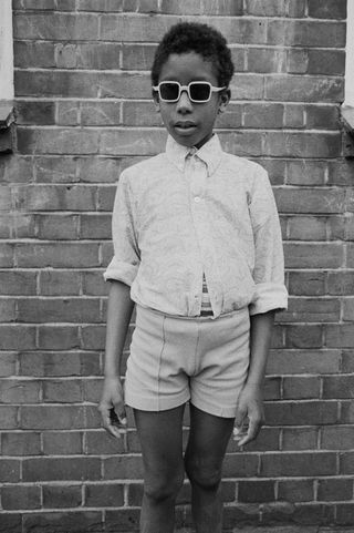 a portrait of a child against a brick wall wearing white shirt and shorts