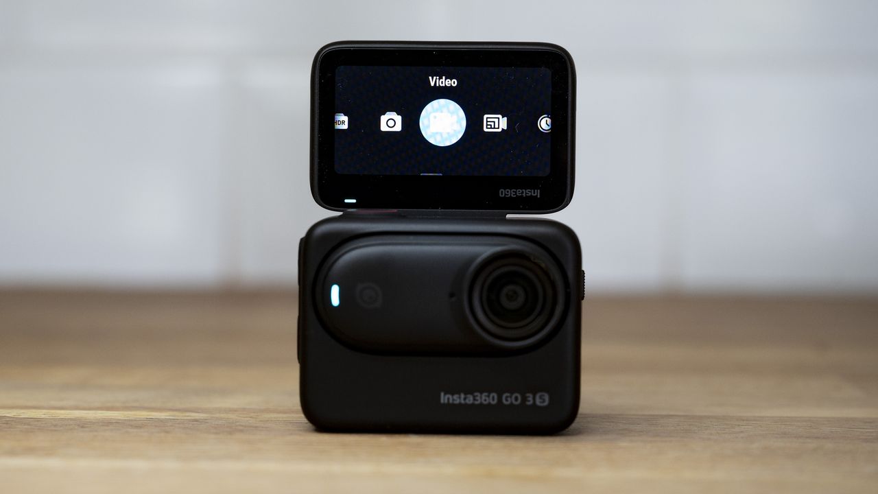 Insta360 Go 3S camera in its housing with rear selfie screen flipped upon a wooden surface