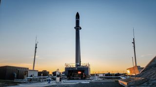 a black rocket stands on the launch pad under a darkening sky