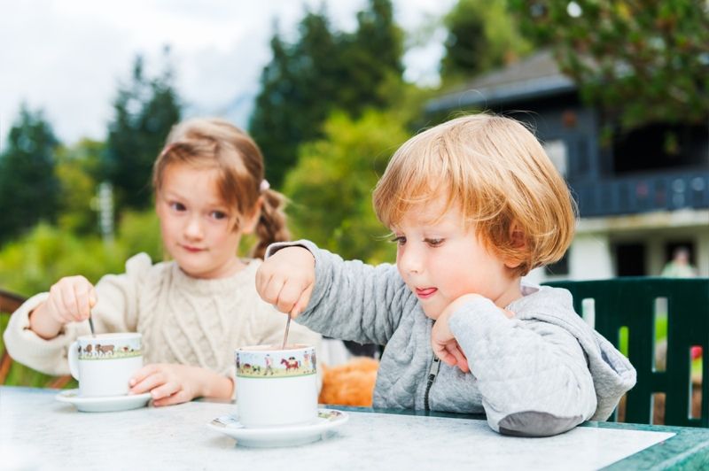 Adorable children drinking hot chocolate outdoors, spending good time on vacation in alpine mountains