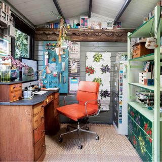 Creative office space inside garden room with vintage furniture and bright orange desk chair