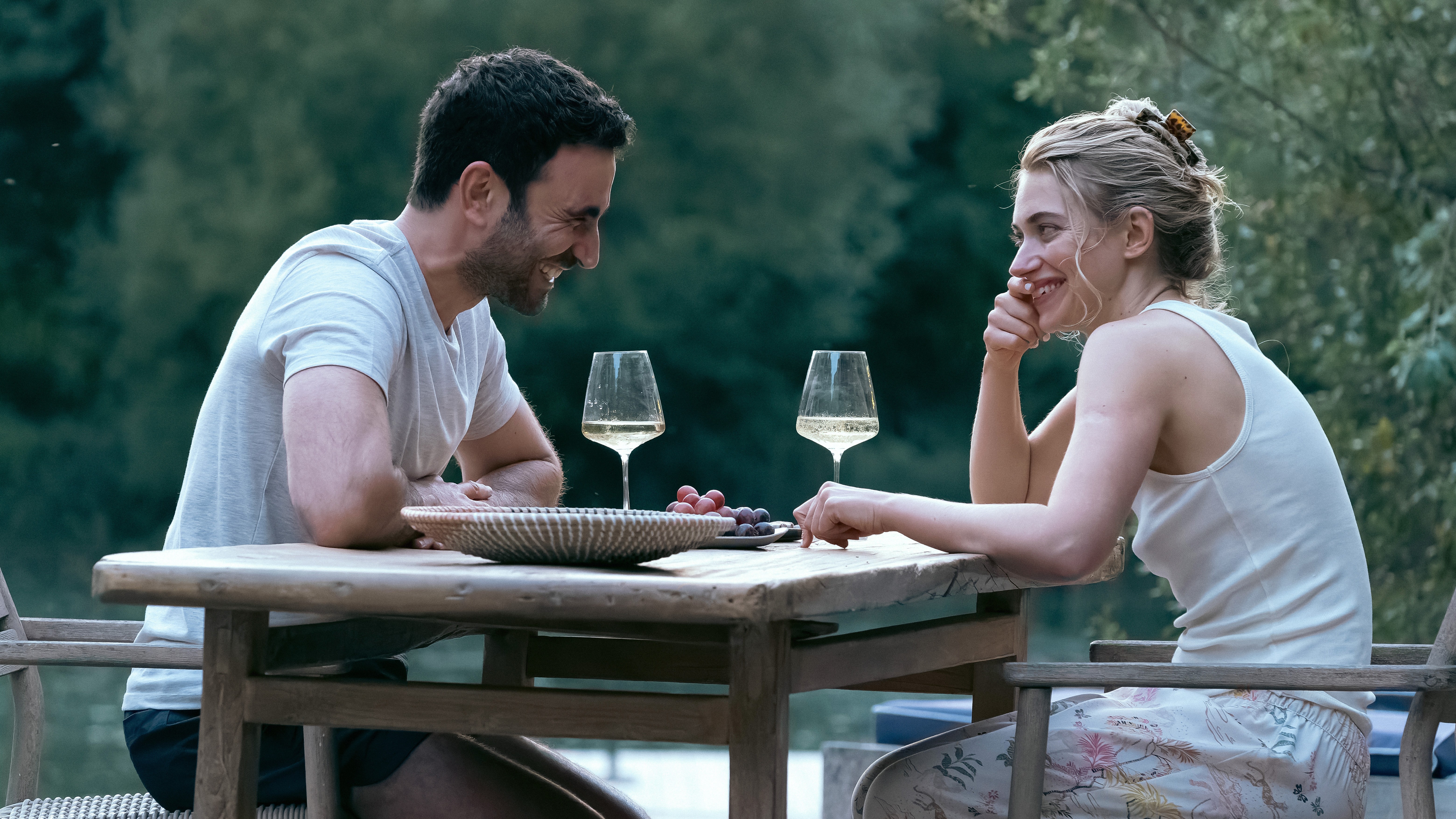L-R: Brett Goldstein and Imogen Poots sit at an outdoor table together in a scene from Apple TV Plus&#039; &amp;quot;All Of You&amp;quot;