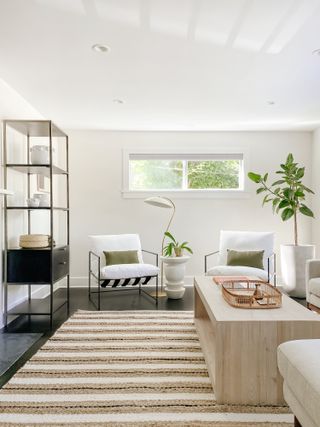 white living room apartment with stripe rug, wooden coffee table, black storage unit, white and metal armchairs, lamps, plants