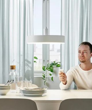 a man dimming the NYMANE Ikea pendant lamp using a remote control, whilst sitting at the dining table