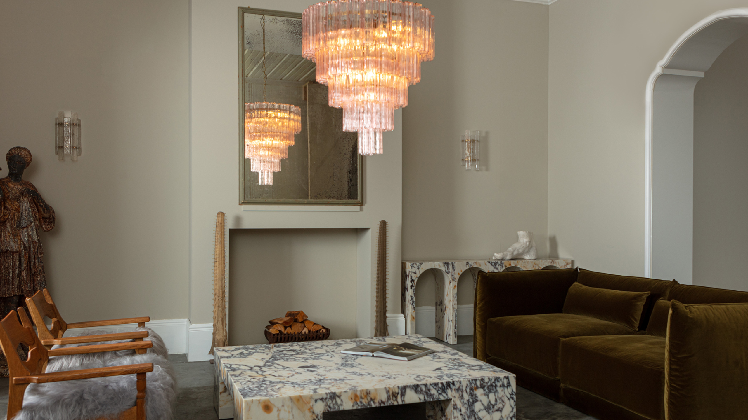 marble coffee table in the middle of a large living room with a glass chandelier hanging above it