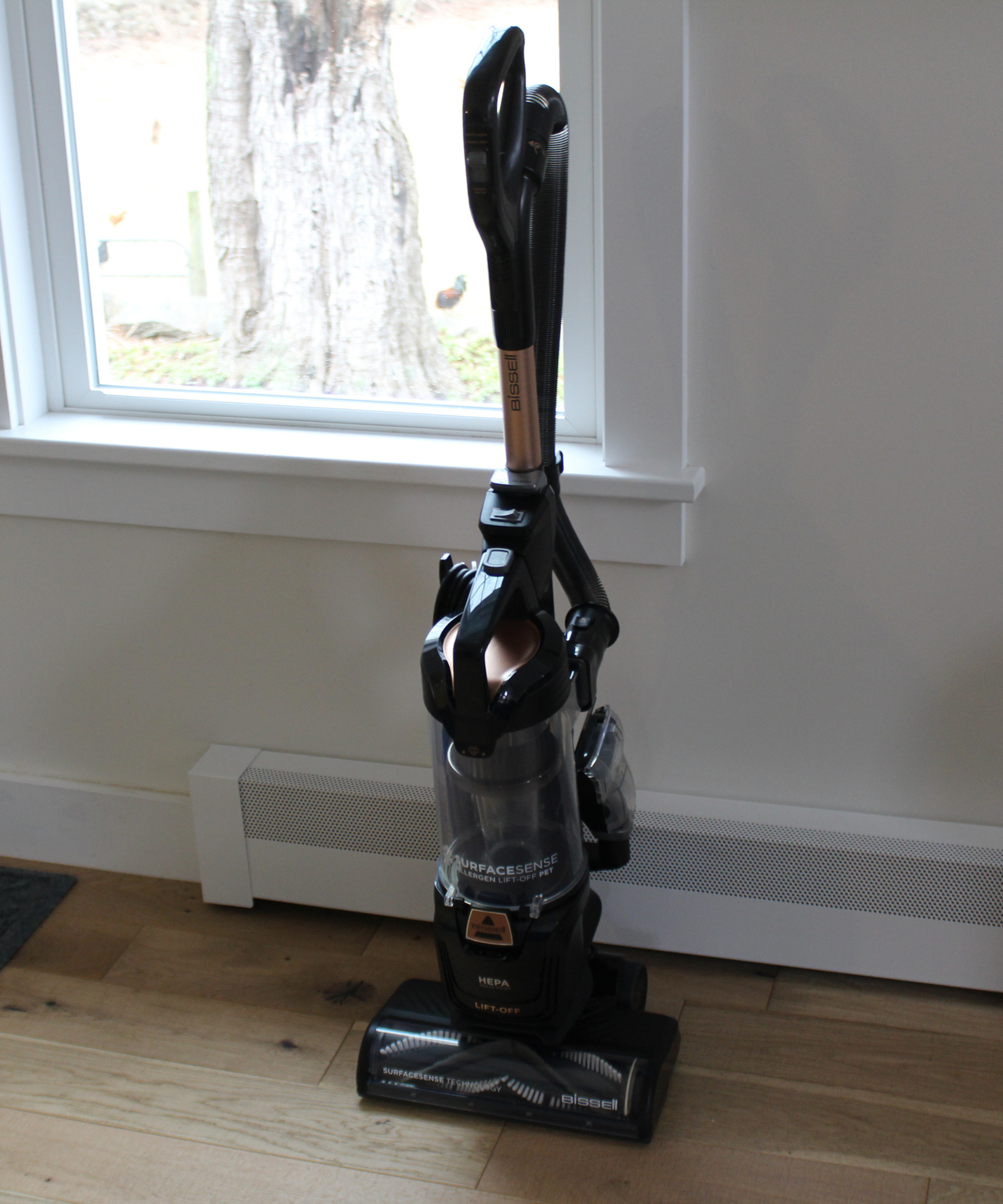 Bissell SurfaceSense Allergen Pet Lift-Off Upright Vacuum stood upright on wooden floor against white wall and window in Camryn's home