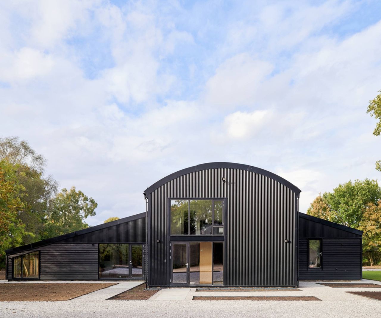 exterior of black dutch barn with central section with curved roof and two sections to side with sloping roofs