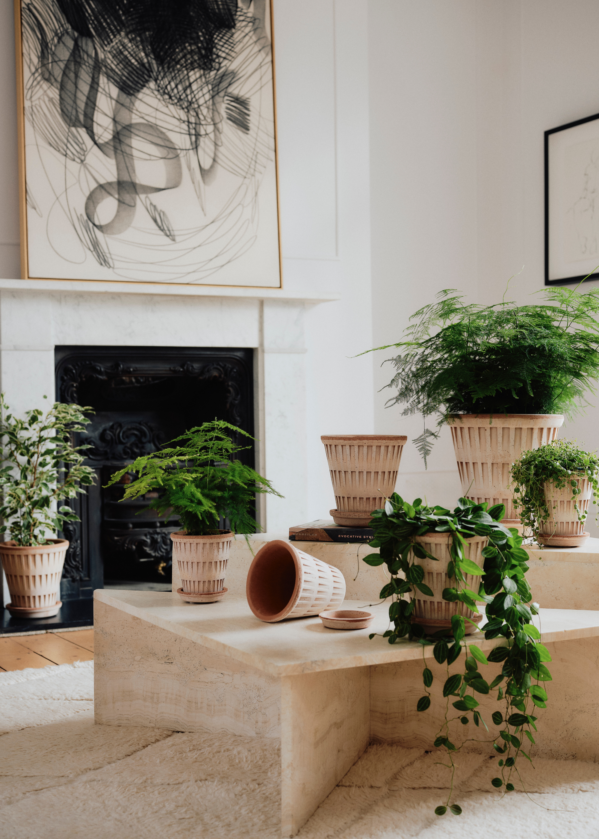 A living room with a marble coffee table with ridged terracotta pots and trailing, feathered houseplants