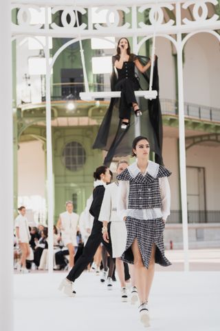 Riley Keough sitting on a swing in the Grand Palais wearing all black Chanel at the Spring Summer 2025 runway show singing "When Doves Cry" by Prince.